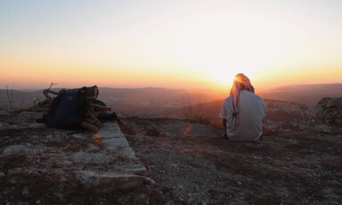 Man sits on rocky outcrop with back to camera 