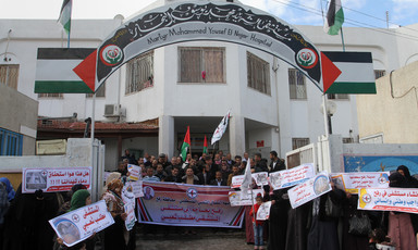 A group of people - some carrying flags and banners - stand outside a building 