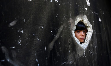 The face of a boy peers through a hole in the wall