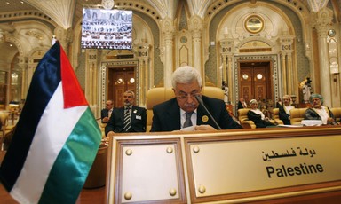 Mahmoud Abbas sits in a gold-themed room behind a sign with Palestine written on it