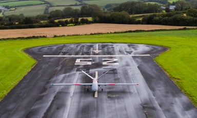 A drone aircraft on a runway surrounded by fields and hills