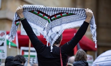 A man holds up a kuffiyeh scarf with a Palestinian flag inlay