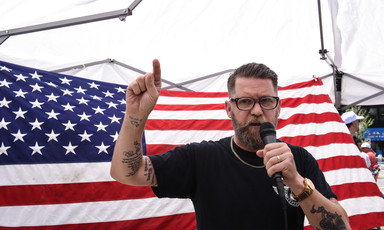 Gesticulating man with microphone stands in front of American flag