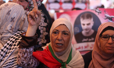 Woman wearing flag as cape, raising finger during protest 