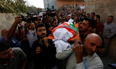 Crowd of men carry shrouded body on stretcher
