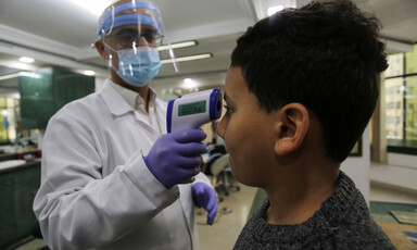 A doctor wearing a face mask is taking a boy's temperature