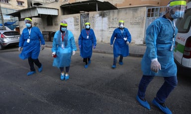 Five nurses in protective gear and masks walk down a street