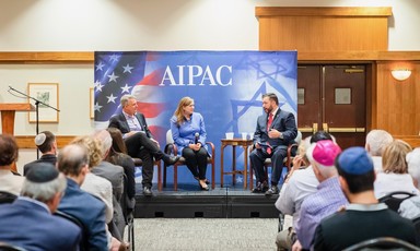Woman and two men sit on podium with AIPAC sign