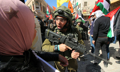 Israeli soldier holding rifle shouts at woman amid crowd
