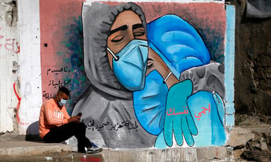 Man wearing mask sits on curb in front of mural showing doctors embracing