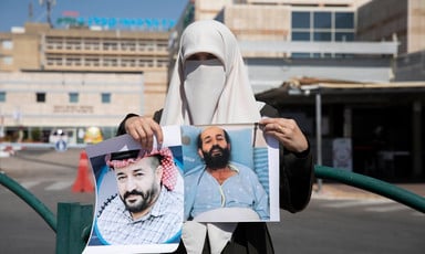 Woman wearing a veil holds two portraits of a man