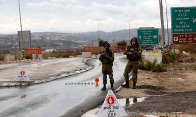 Two heavily armed soldier stand on the side road