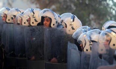 Police officers wearing helmets hold riot shields 