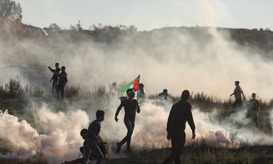 Protesters, one of them carrying a Palestine flag, are silhouetted against clouds of smoke