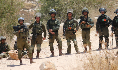 Several Israeli soldiers holding guns stand in a row