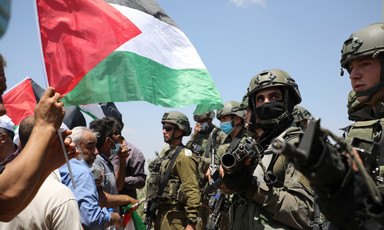 A Palestine flag waves in front of Israeli soldiers