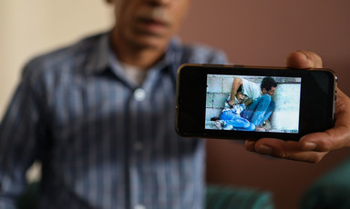 A man holds out a mobile phone showing a still from grainy video footage