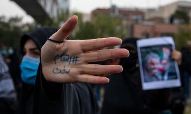 Woman holds hand up as others stand nearby with posters