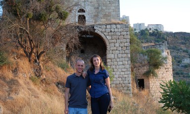 Couple stand in front of abandoned stone building on slope
