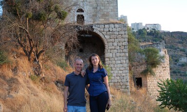 Couple stand in front of abandoned stone building on slope