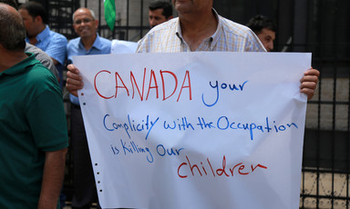 Man holds sign reading Canada your complicity with the occupation is killing our children