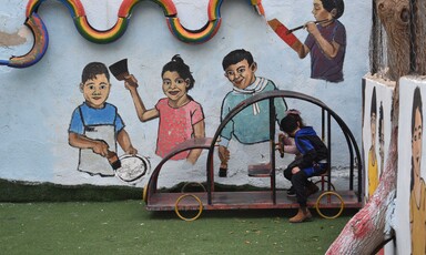 Children play outside in front of a brightly painted wall