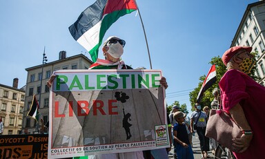 A protester holds a Palestine flag and a banner that reads Palestine Libre