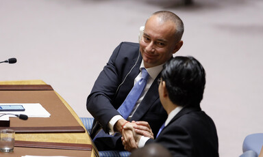 Smiling man seated at table shakes hands with man whose back is turned toward camera