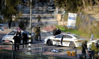 Covered body lies on road surrounded by police vehicles and uniformed personnel