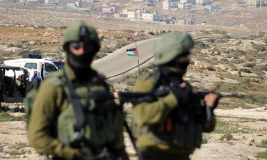 Two armed and uniformed soldiers stand in front of road