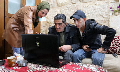 Two men and a woman stare at a laptop