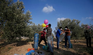 A group of men stand in a field of trees with a number of colorful balloons