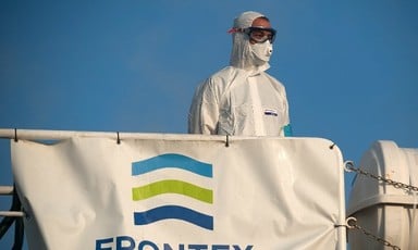 Man wearing mask and other protective equipment stands behind Frontex banner