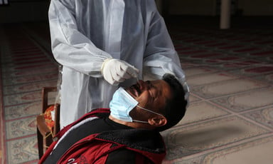 A man flinches as a medical worker in full protective gear swabs his nose