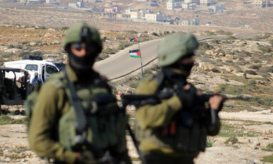 Two Israeli soldiers with Palestinian flag in background 