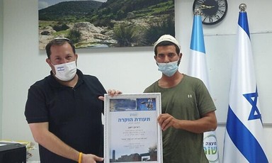 Two men wearing face masks hold framed certificate