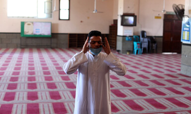 A man raises his hands to his head in prayer