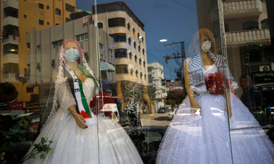 Two mannequins in wedding dresses and face masks are seen through through a shop window