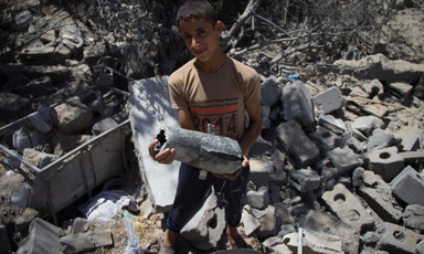 Boy holding metal object stands amid rubble