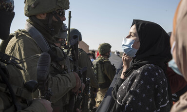 Palestinian woman wearing surgical mask faces an armed Israeli soldier