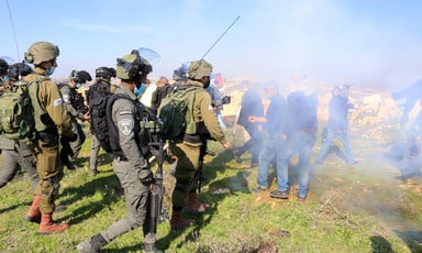 Uniformed soldiers face off against unarmed protestors hidden by a cloud of tear gas