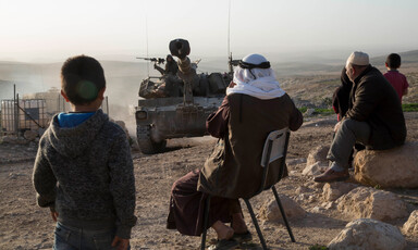 Villagers watch an approaching military vehicle  