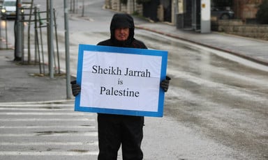A person wearing a winter coat holds a sign in the street 