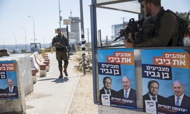 A soldier stands at a concrete checkpoint plastered with posters
