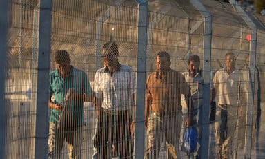 A group of men walk behind a metal fence