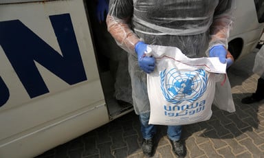 Man seen from chest down holds bag of UNRWA food aid in front of UN vehicle