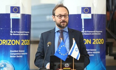 Emanuele Giaufret stands at podium with EU and Israel flags