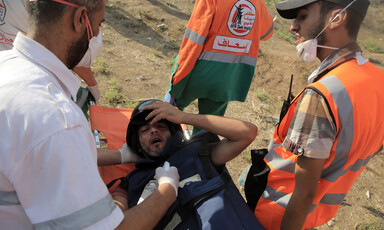 A wounded man wearing a press helmet and flak jacket is carried on a stretcher