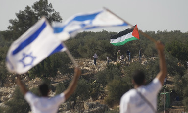 Two people wave Israeli flags opposite of a group with a Palestine flag in an olive orchard