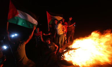 Young men smile while holding flags and standing next to a fire at night